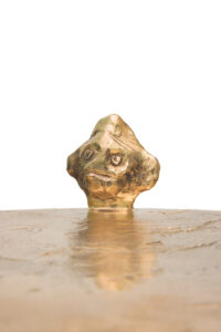 Close-up of the tray of the Golden Him table by Elizabeth Garouste in gold bronze, from which a small serious head emerges in its center